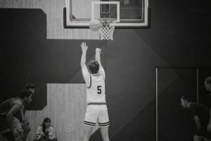 Svartvit bild på basketspelare som kastar boll mot korg i en hall.
