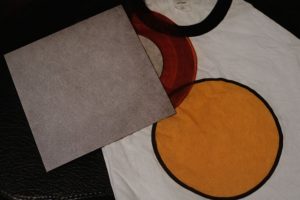 T-shirt med runda tryck i rött och gult samt ett grått papper på svart bakgrund.