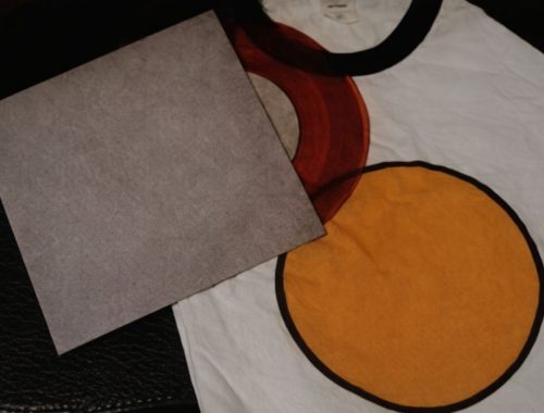 T-shirt med runda tryck i rött och gult samt ett grått papper på svart bakgrund.