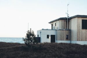 Träklätt kusthus med stora fönster intill havet och vindutsatt mark