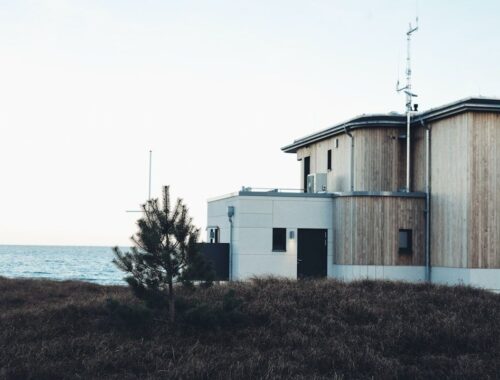 Träklätt kusthus med stora fönster intill havet och vindutsatt mark